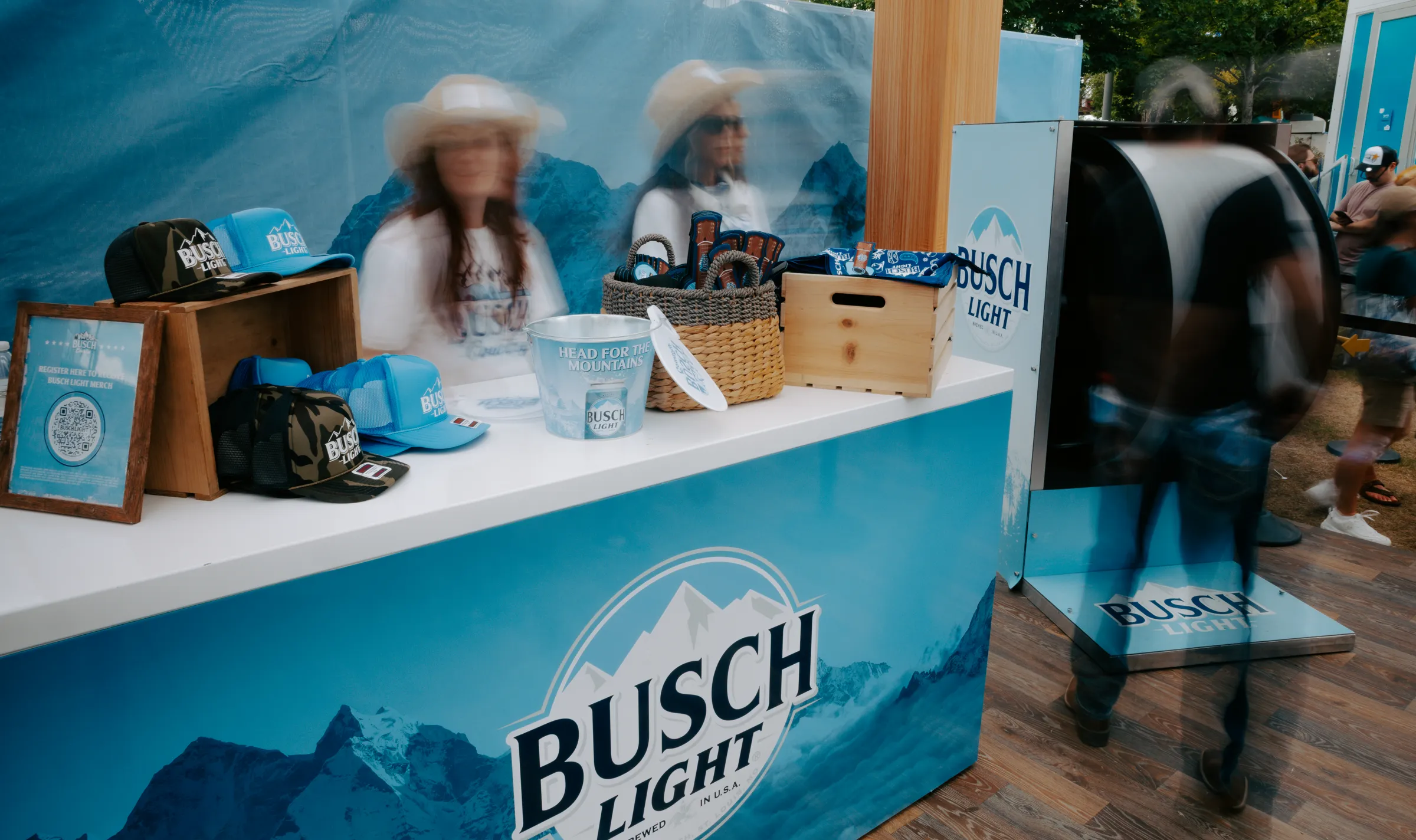 Merch counter with hats, bandanas and koozies against a mountain-print backdrop