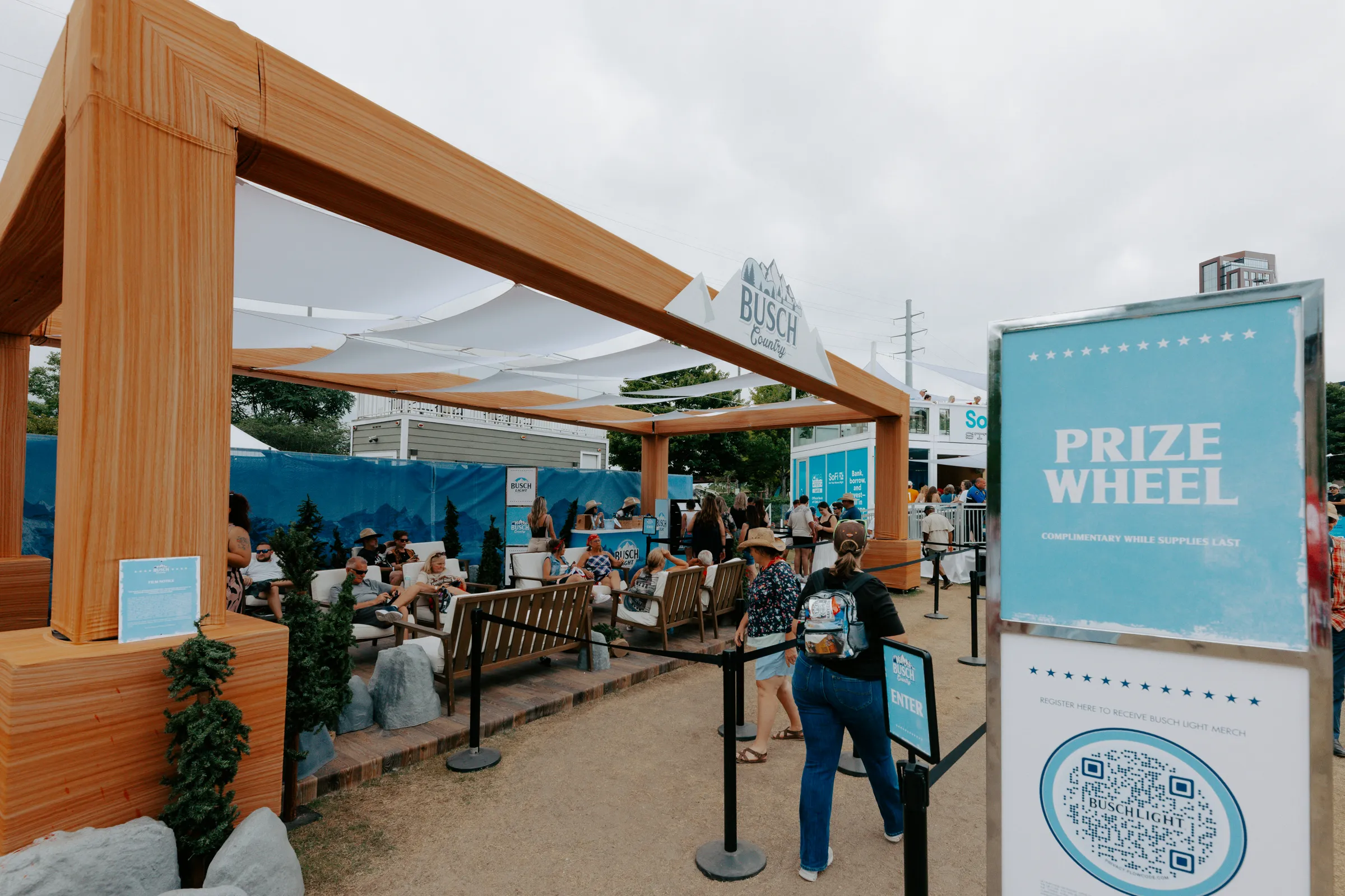 Timber pergola lounge with mountain-print scrim walls and a prize wheel sign at the entry
