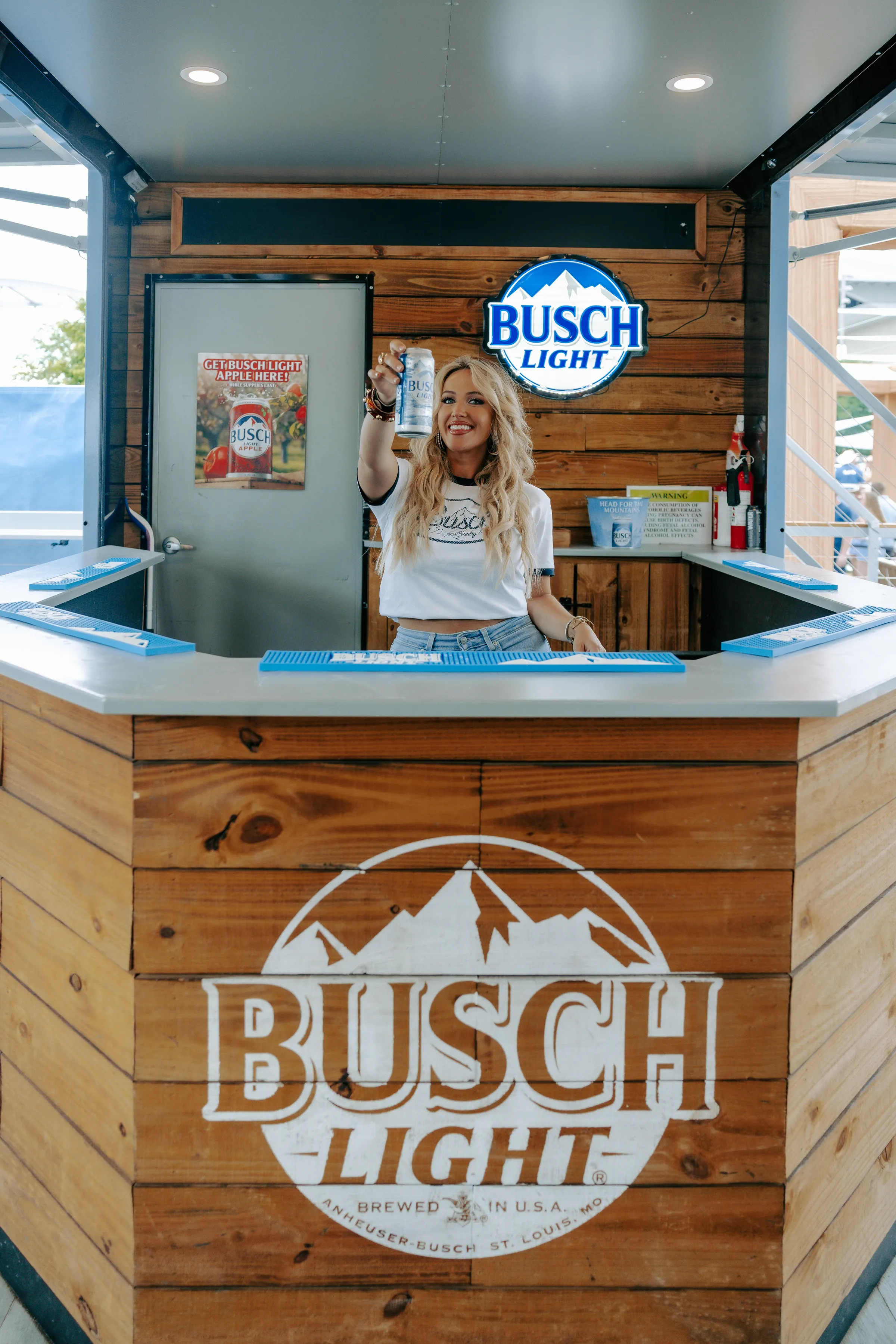 Bartender raising a can inside the timber Busch Light bar build with a lit logo sign
